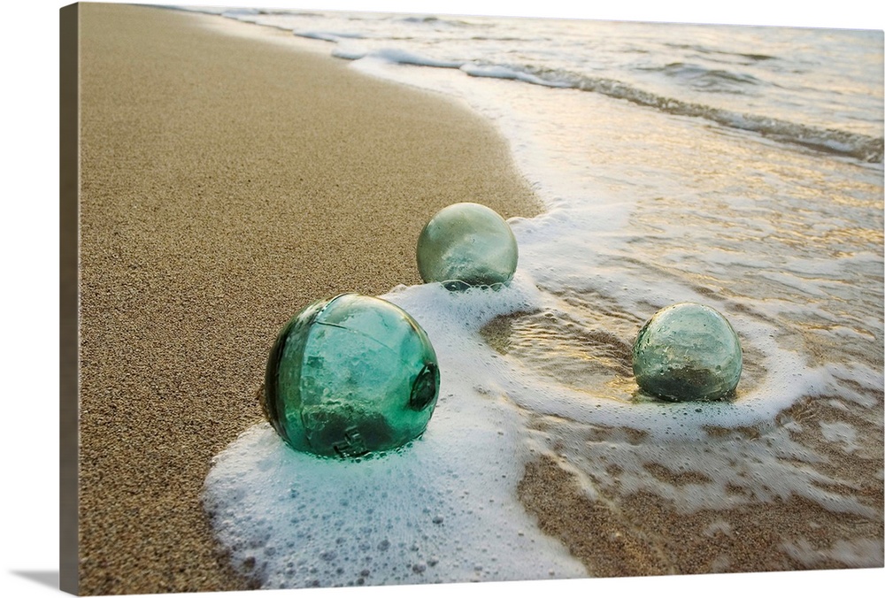 Three Glass Fishing Floats Roll On The Sandy Shoreline with Ripples of Water and Seafoam | Large Canvas Art Print | Great Big Canvas
