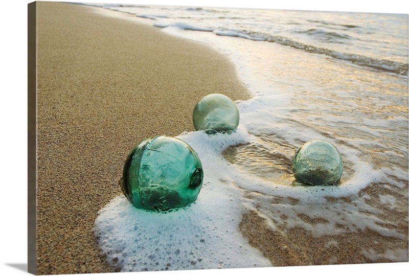 Three Glass Fishing Floats Roll On The Sandy Shoreline with Ripples of Water and Seafoam | Large Metal Wall Art Print | Great Big Canvas