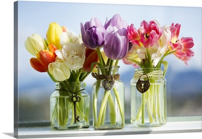Tulips in glass vases with decorative pendants on the window sill with the city behind