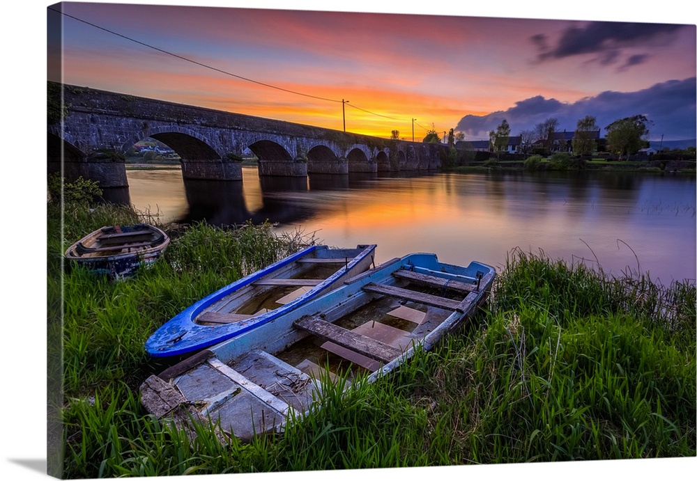 Two small wooden boats on the bank of the Shannon river in front of a stone bridge at sunset in summer; O'Brien's Bridge, ...