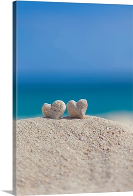Two white heart shaped coral rocks placed together on sand at the beach