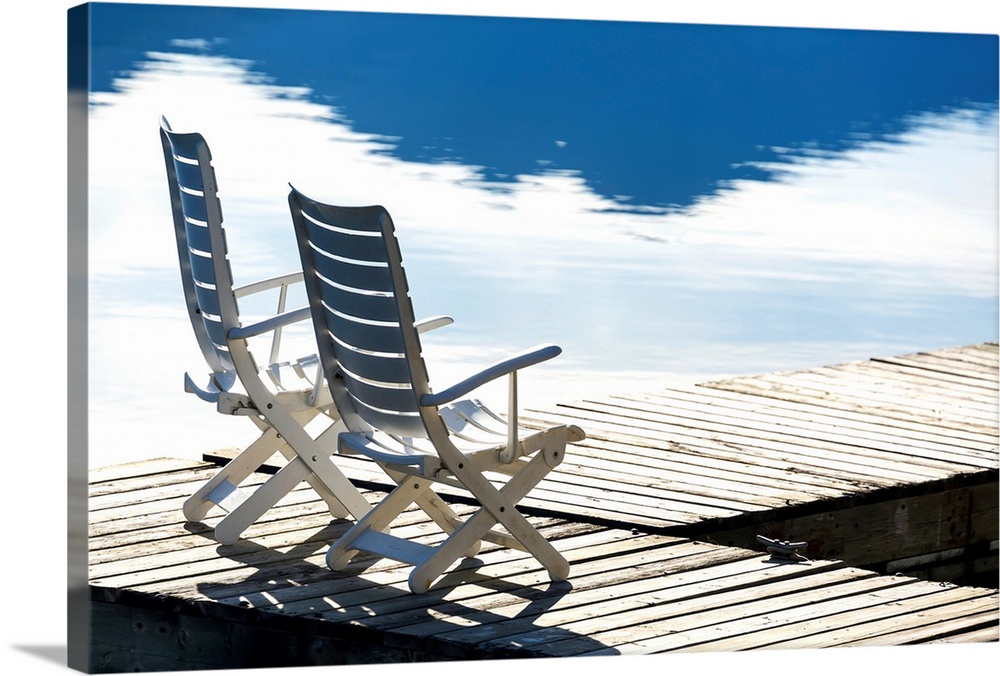 Two white wooden deck chairs on wooden boat dock reflecting in the water; Invermere, British Columbia, Canada