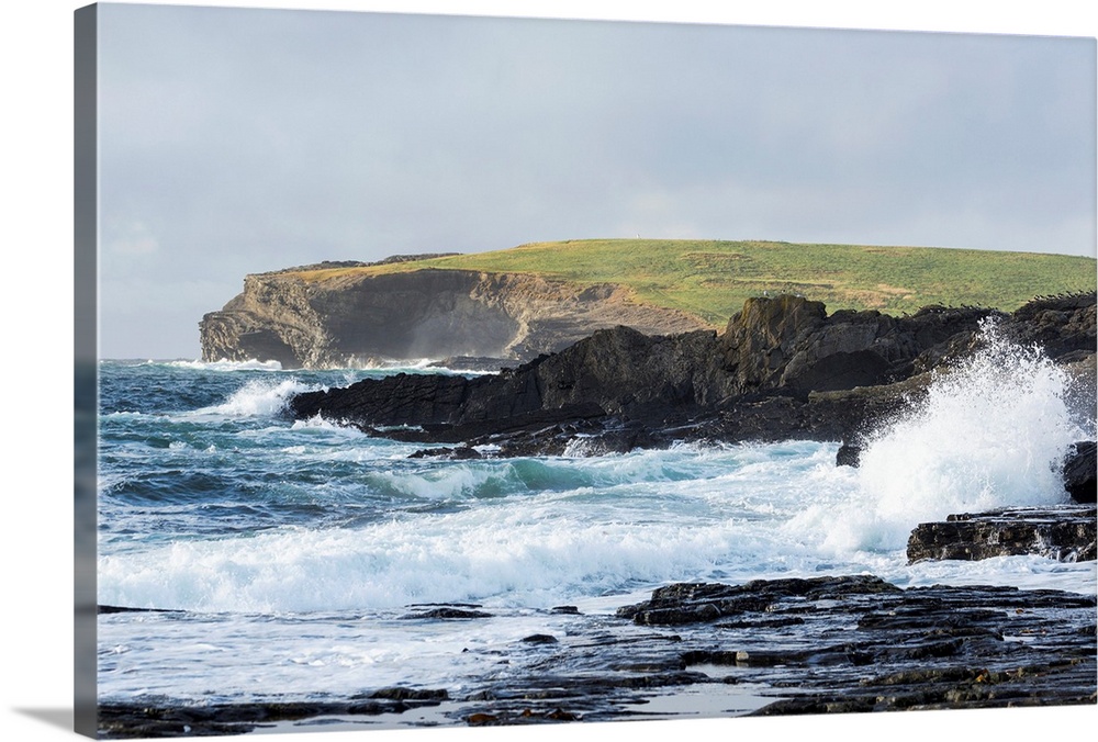 Waves crashing into rocky coast with large grassy hill and cliffs in background, Kilkee, County Clare, Ireland.