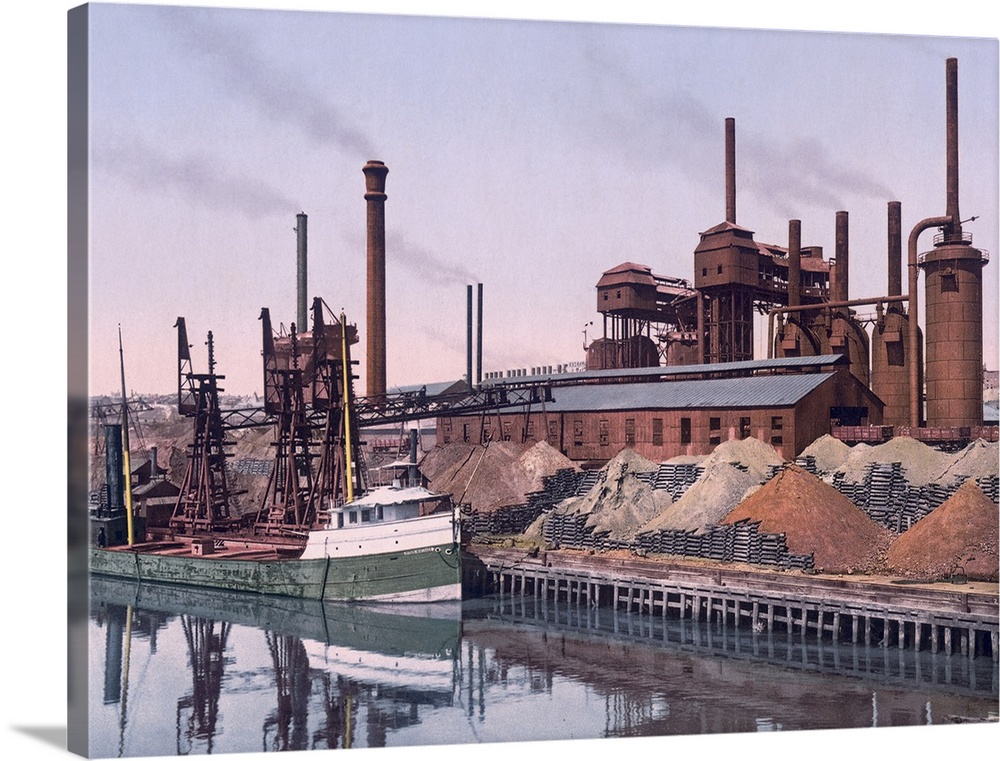 Vintage color photo of an American Steel factory on the banks of a river with tall smoke stacks and piles of minerals.
