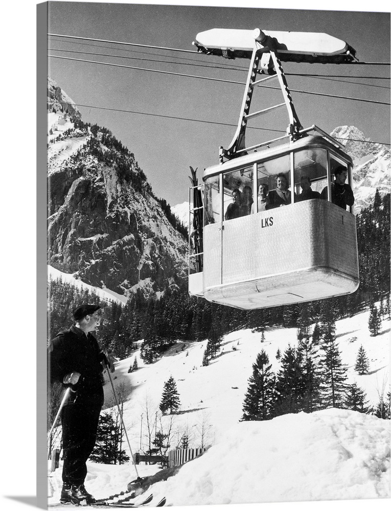 A group of tourists ride up a ski slope in a cable car in the Alps, Switzerland, 1950s