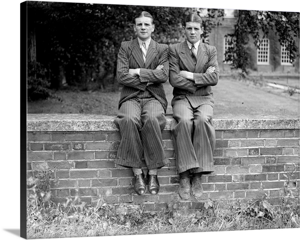 1938:  Twins in pinstripe suits sit on a wall, their arms identically crossed