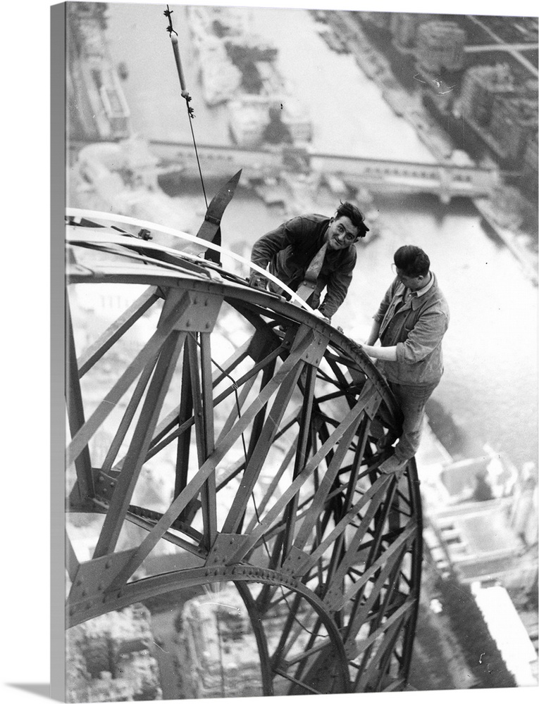 High above the River Seine two electricians work on the lights on the Eiffel Tower which will illuminate the Paris Exhibit...
