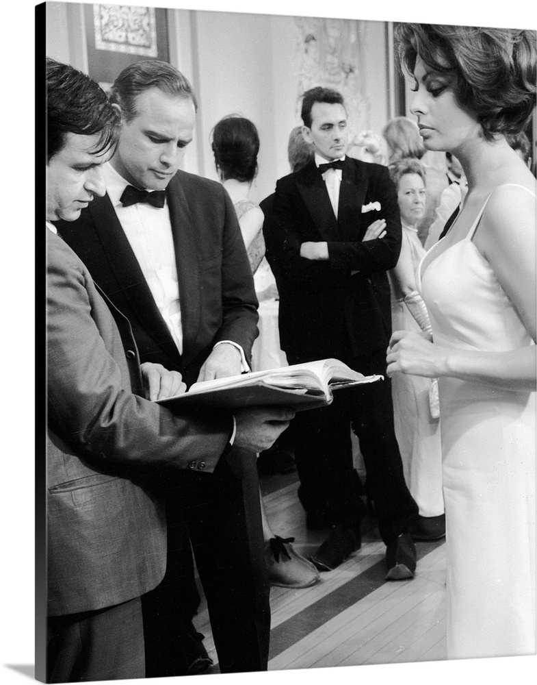 April 1966:  American film star, Marlon Brando, checks his script whilst Sophia Loren looks on, during the filming of 'The...