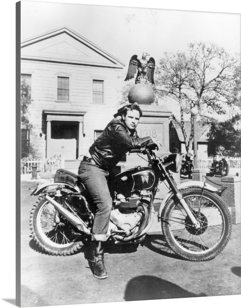 Burly American actor Marlon Brando sitting astride his motorbike in a scene from the classic film 'The Wild One', directed...