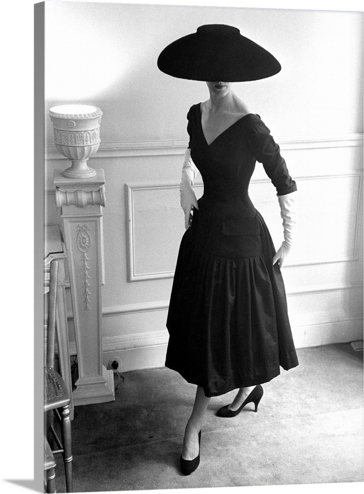 A model wearing a black cocktail dress and a black velvet wide-brimmed hat, designed by Ronald Paterson  Original Publicat...