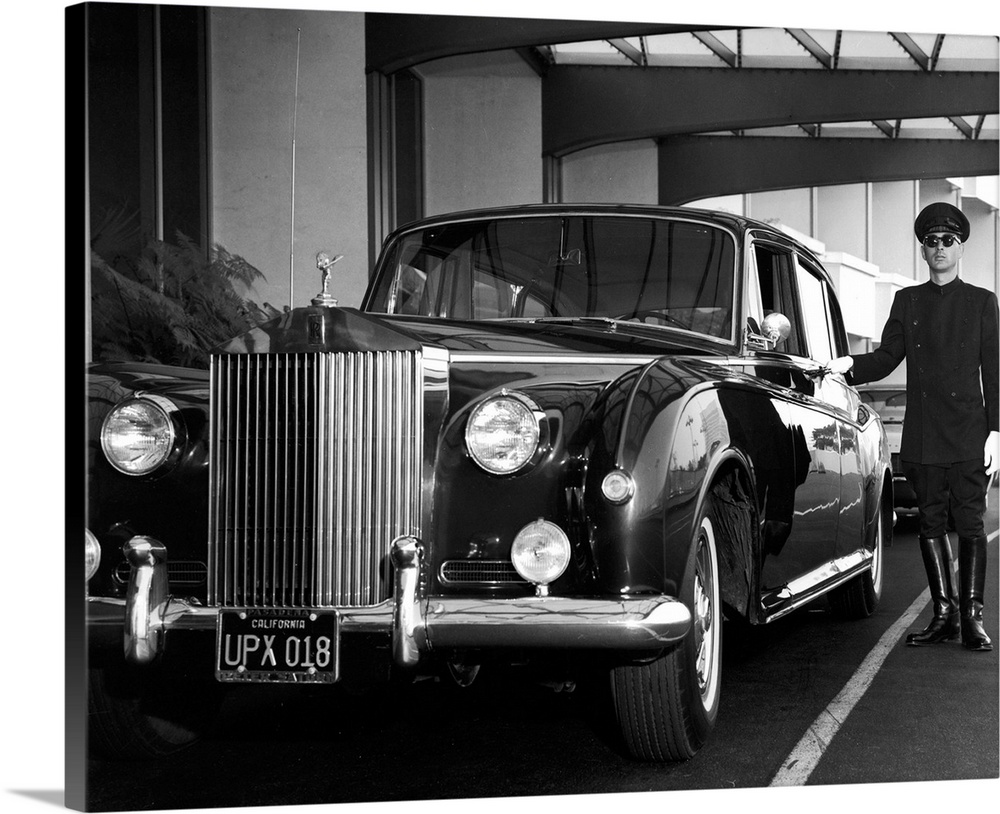 A uniformed chauffeur waits beside a Rolls-Royce Phantom V, California, circa 1959