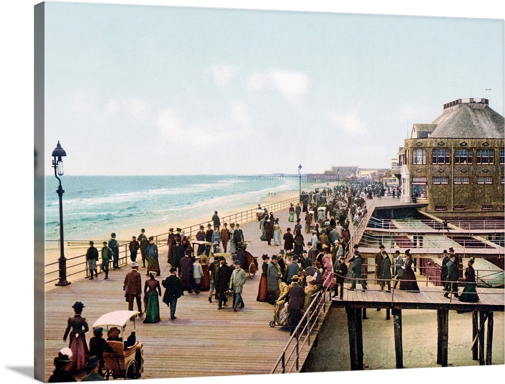 Old photograph of well-dressed people walking along the Atlantic City Boardwalk in New Jersey. Seaside buildings and the o...