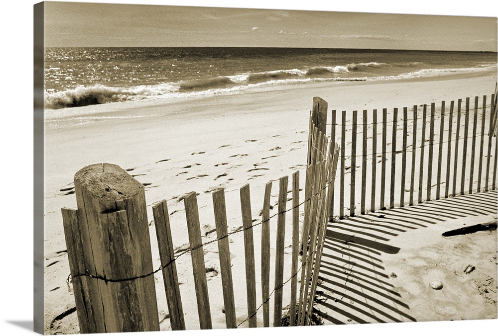 Sepia toned photograph of a sand dune fence casting long shadows on a sandy beach.