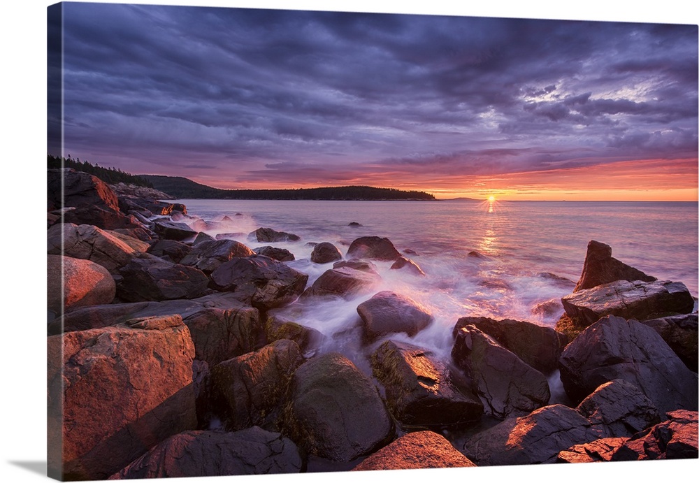 Photograph of the coast of Acadia Maine with the sun setting under purple clouds in the distance.