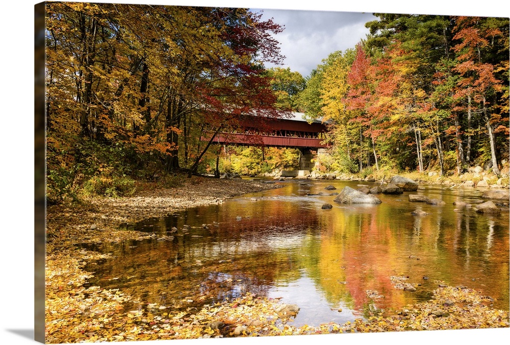 A photograph of a covered bridge spanning a stream in a forest in autumn foliage.