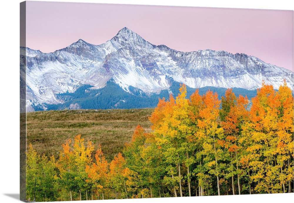 Beautiful, bright landscape photograph of colorful Fall trees in the foreground, snowy mountains in the background, and a ...