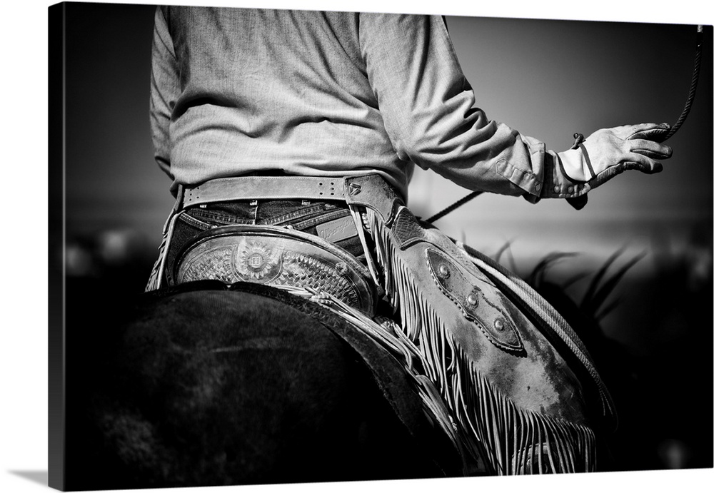 Black and white photograph of the back of a cowboy on horseback swinging his lasso.