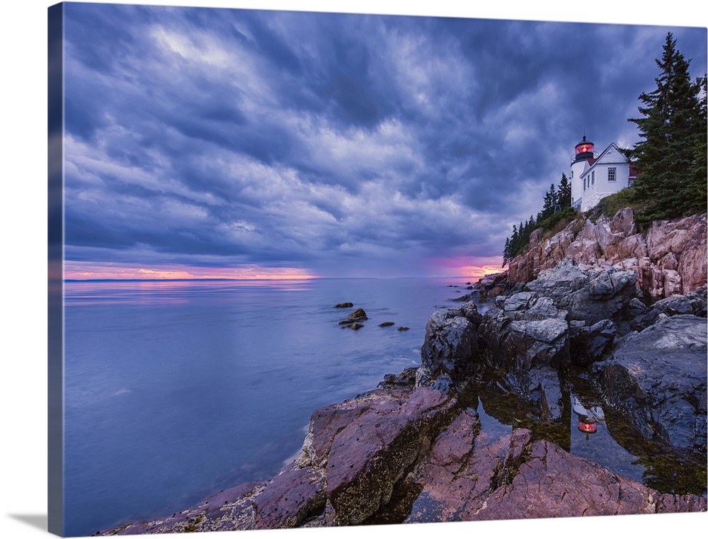 Photograph of a white lighthouse on the coast of Maine, with the sun setting under big textured  fluffy clouds.