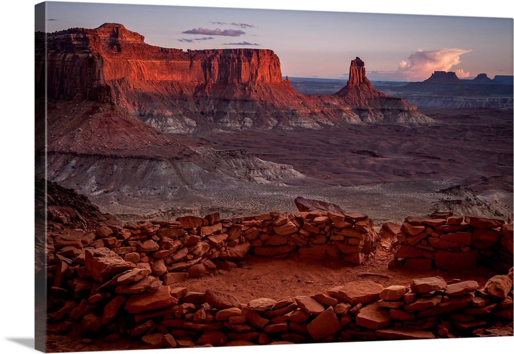 Landscape photograph of stacked rocks creating a circle with canyons in the background at sunrise.