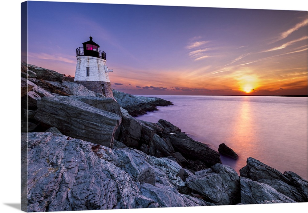 Long exposure photograph of a lighthouse on a rocky cliff with a beautiful sunset over the water.