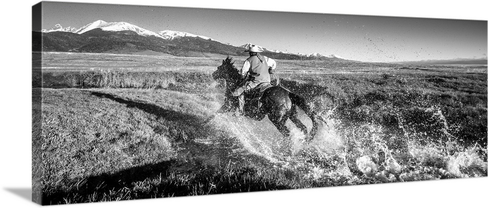 Black and white action photograph of a cowgirl riding her horse through a stream.