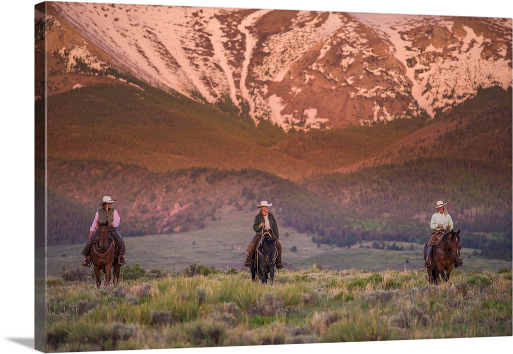 Photograph of three people on horseback in a row with snow covered mountains in the background.
