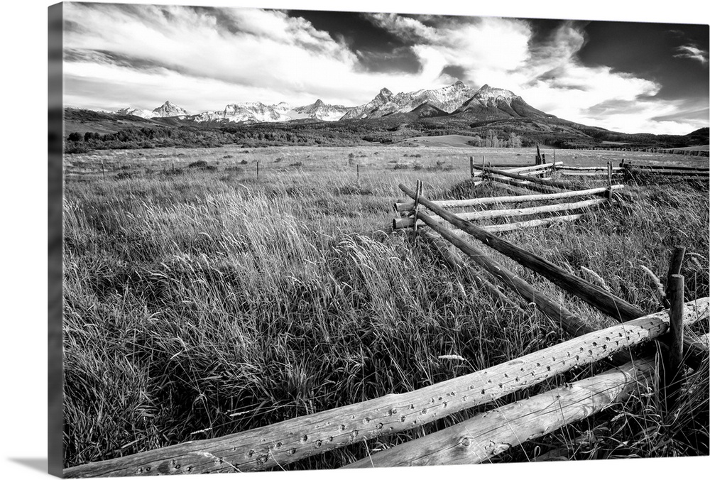 Black and white landscape photograph of a field with tall grass and a wooden fence creating leading lines to the mountain ...