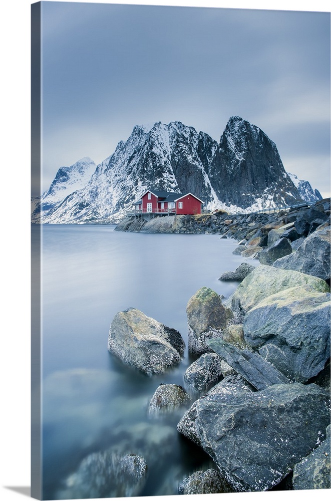 A photograph of a Norwegian red cabin with gray mountain boulders all around.