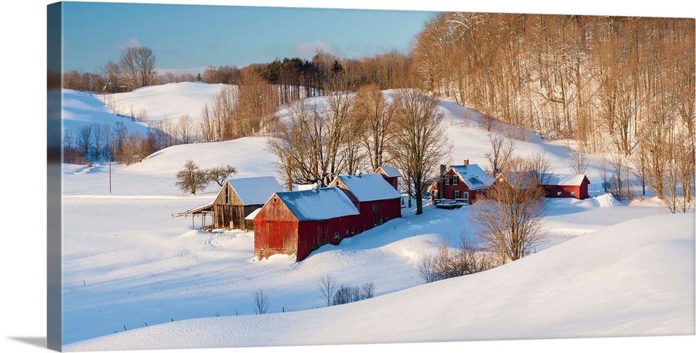 Landscape photograph of snowy farmland with red buildings and bare trees in Winter.