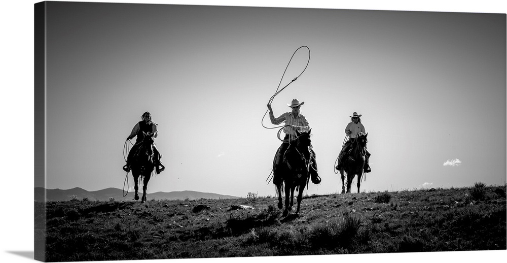Black and white photograph of three cow girls on horseback with their lassos out.