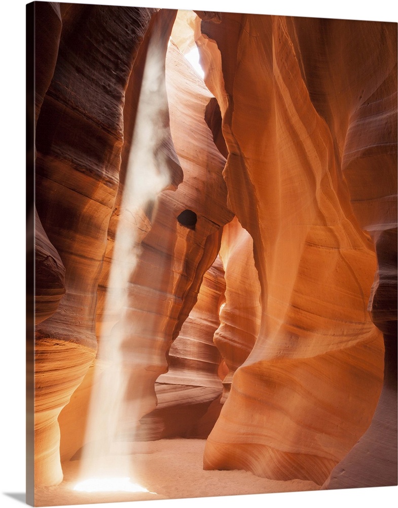 An artistic photograph of a slot canyon with a shaft of sunlight piercing the crevasse above.