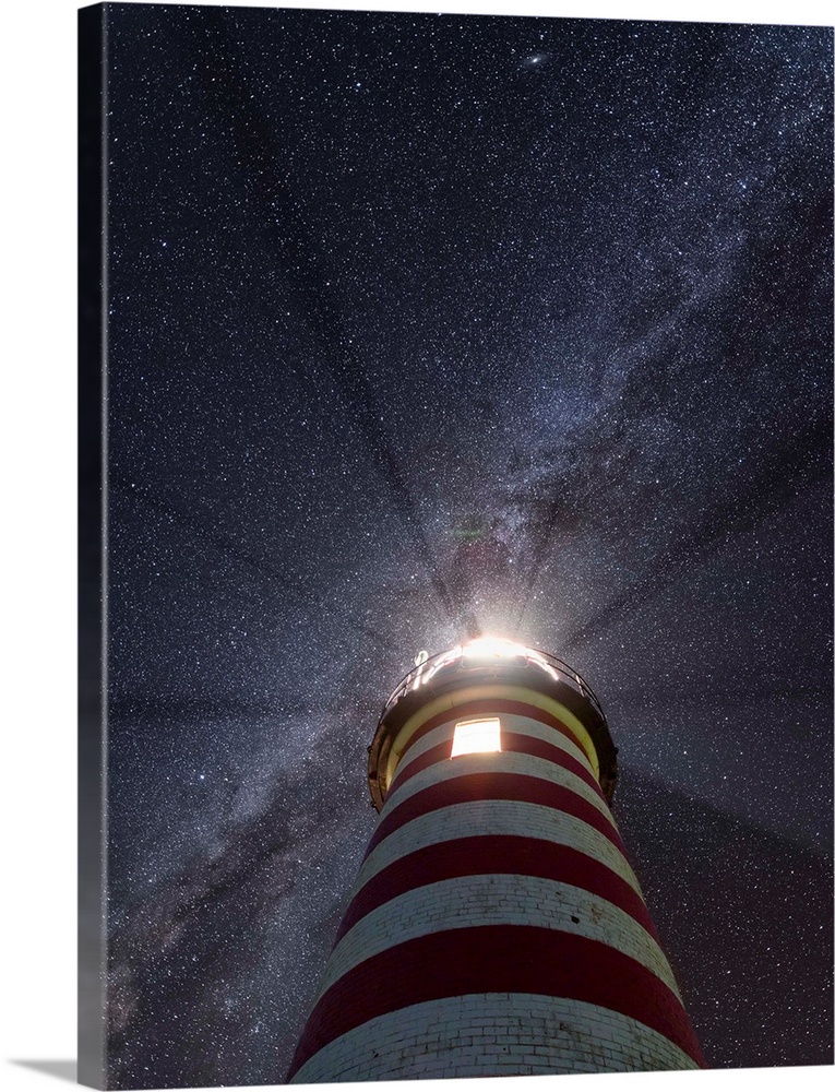 Photograph looking up at a red and white striped lighthouse to a purple and blue starry sky with the Milky Way running dia...