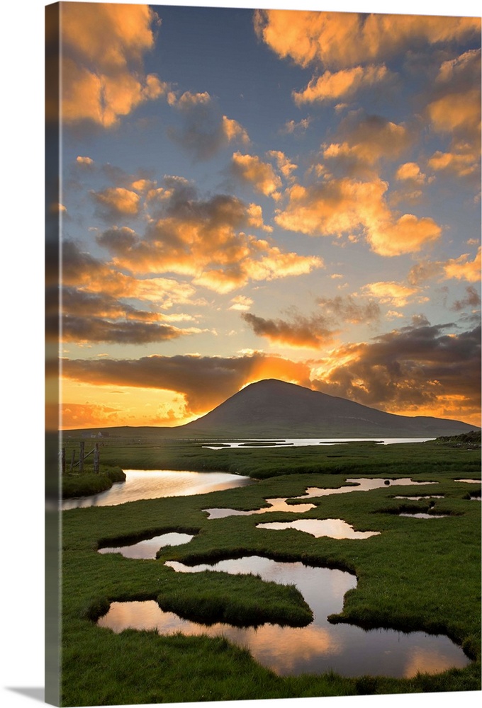 Landscape photograph of a sunrise beaming though a mountain with a marsh in the foreground.