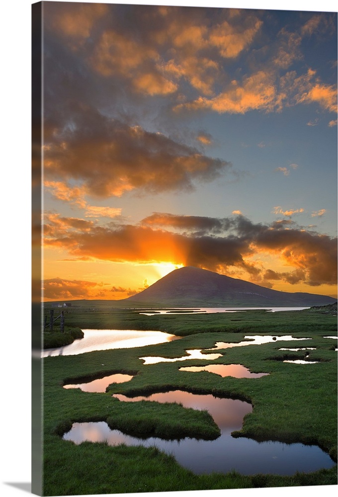 Landscape photograph of a sunrise peaking though a mountain with a marsh in the foreground.