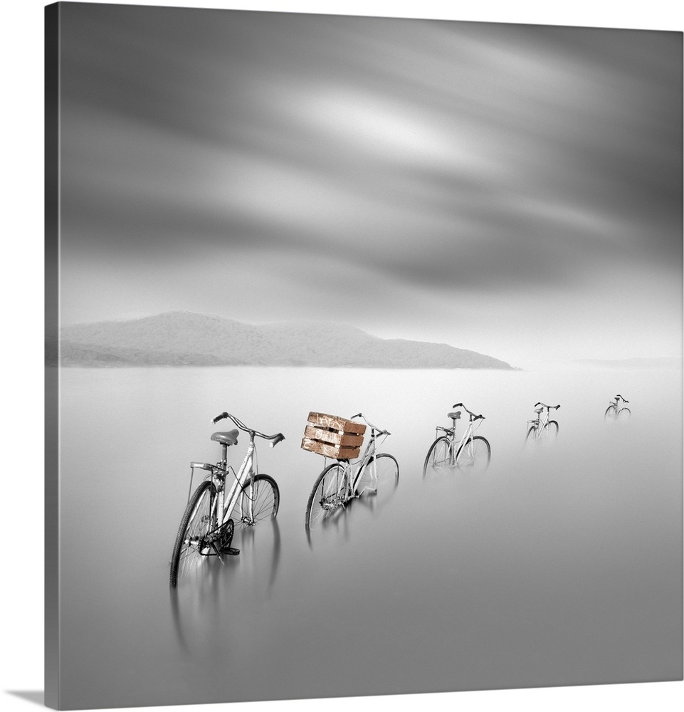 Artistic photograph of a line of bicycles standing unattended in a shallow water with streaking clouds overhead.