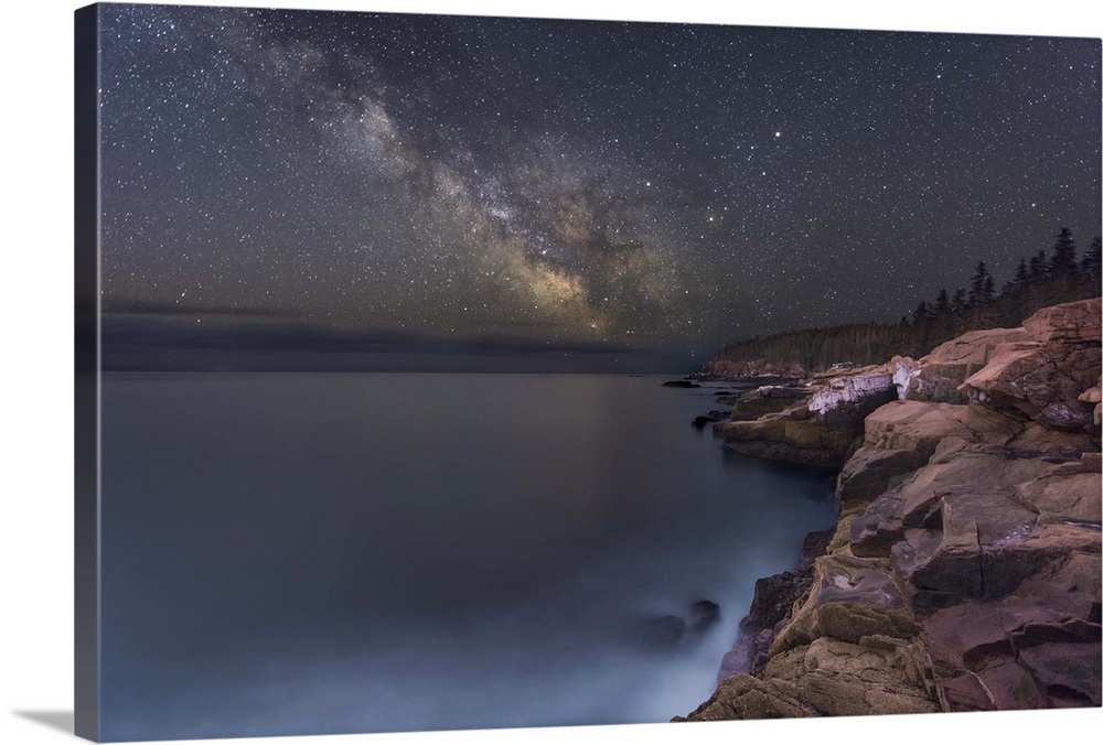 A photograph of a rocky coastline under a starry night sky.