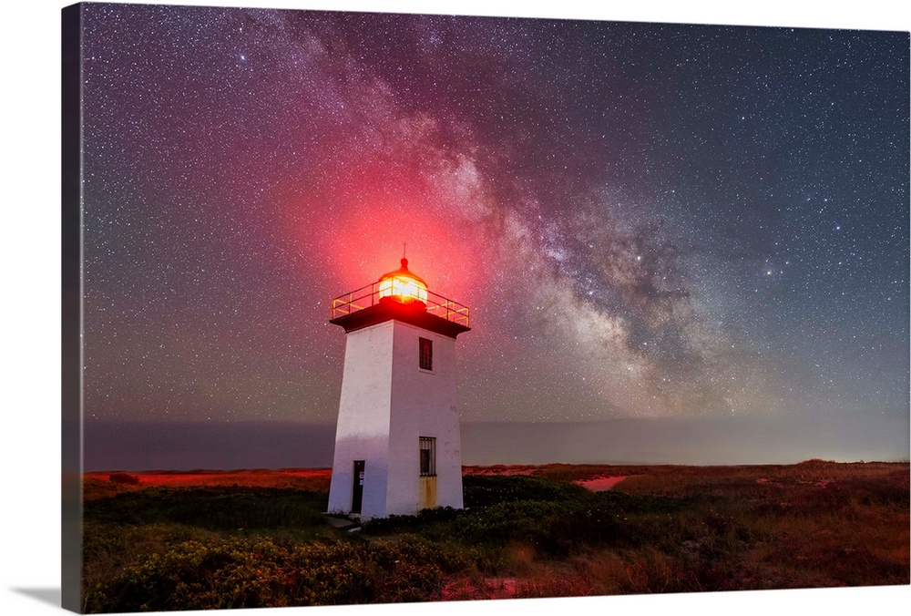 Landscape photograph of a white lighthouse underneath the milky way with a shining red light at the top.