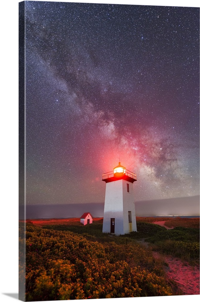 Photograph of a white lighthouse with a red light shining on top with the Milky Way in the sky above.