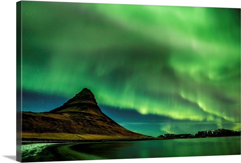 A photograph of an Icelandic landscape with a mountain peak seen under the northern lights illuminating the sky.