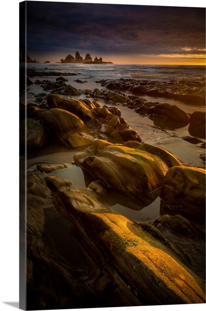 Golden lit photograph of a rocky beach shore at sunset.
