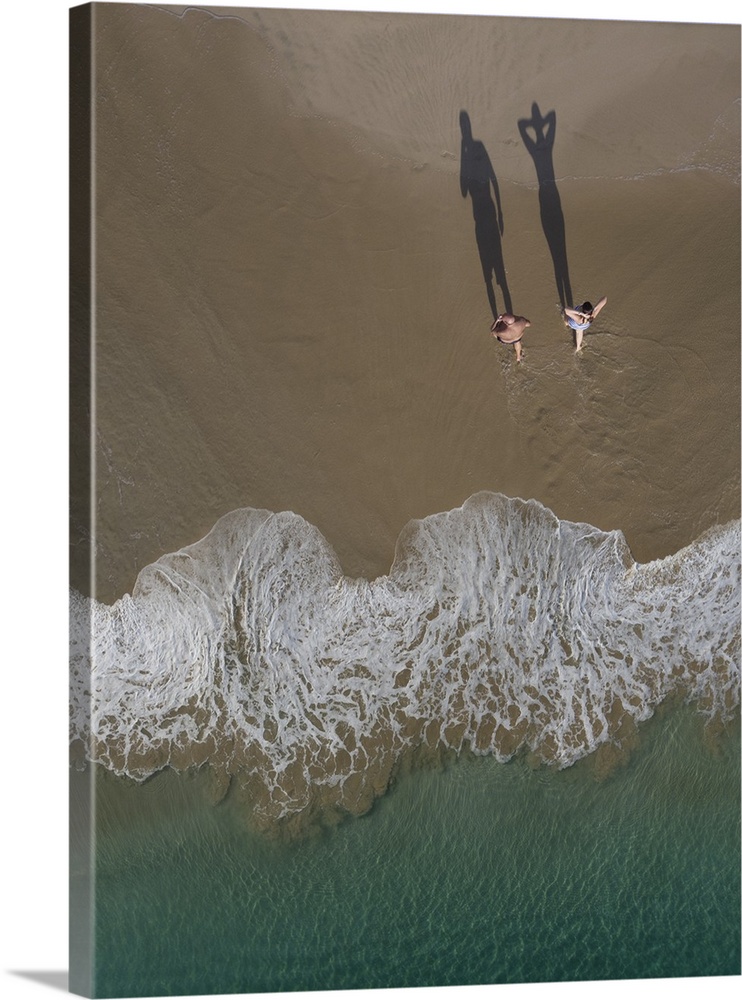 An artistic photograph of an aerial view of two people on a beach casting long shadows.