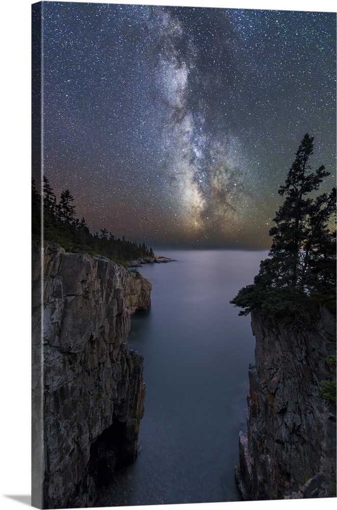 Landscape photograph of two cliffs with water in between them at night with the Milk Way in the sky above.