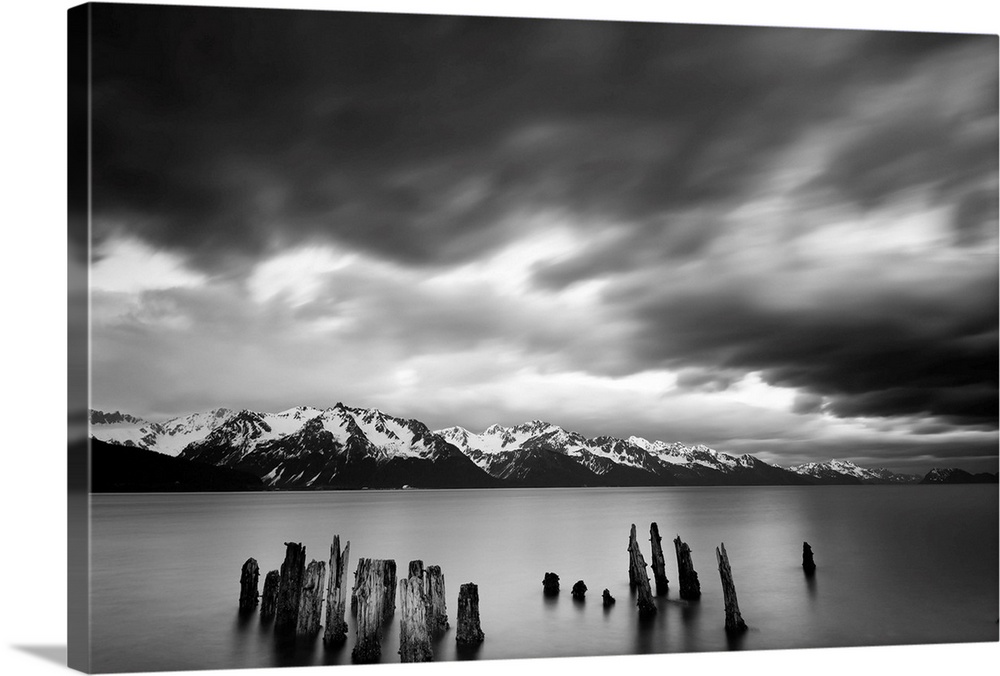 Long exposure black and white landscape photograph of a quiet lake with snow capped mountains in the distance.