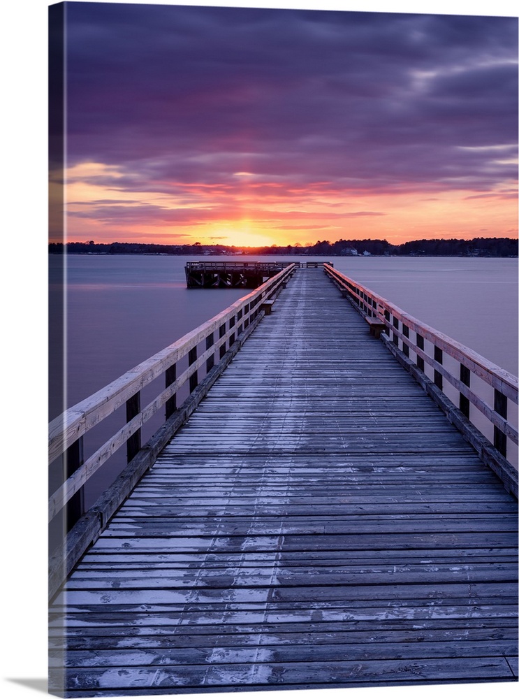 Photograph of a long, wooden pier at Fort Foster, Maine, with a pink and purple sunrise.