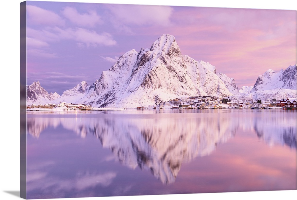 A photograph of a snow covered mountain range in winter casting a clear reflection in the fjord below.