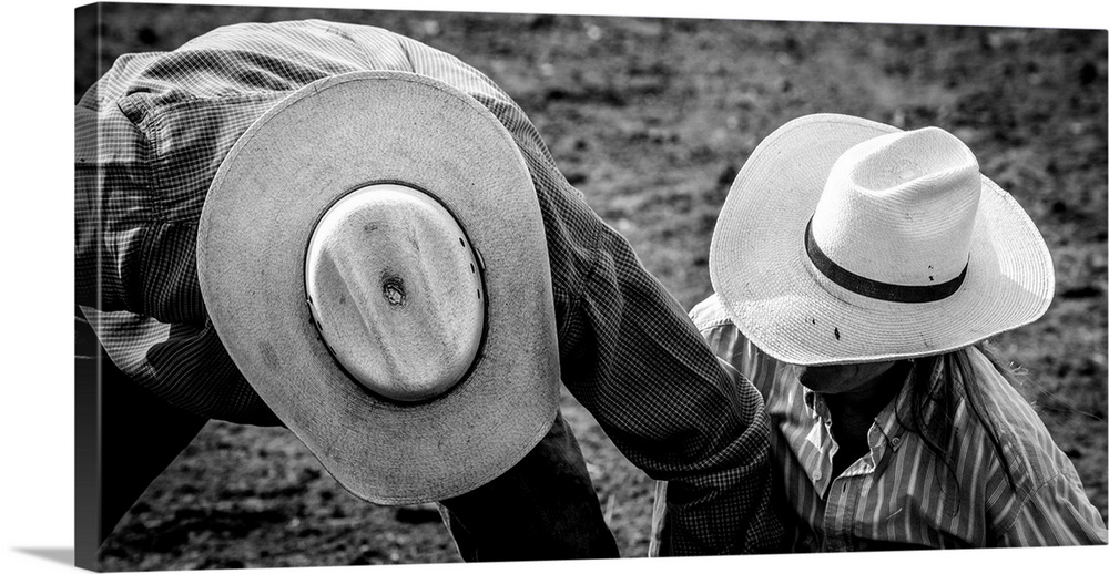 Black and white photograph of two people wearing cowboy hats on the ground at a rodeo.