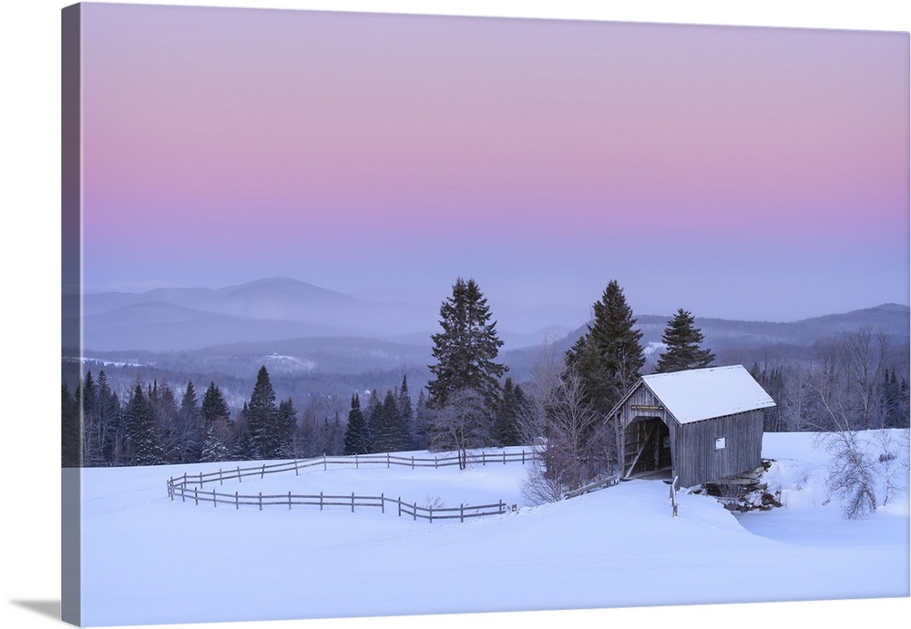 Landscape photograph of a rural Winter scene with fog covered mountains in the background and a blue, pink, and purple sun...