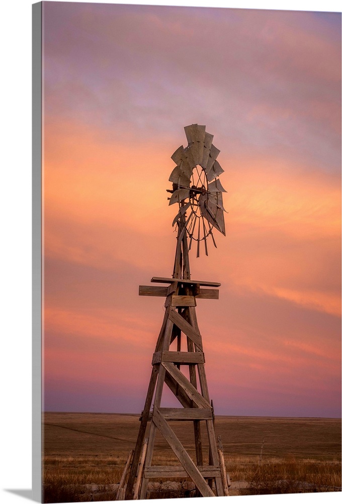 Photograph of a wooden windmill in the middle of a field at sunset.