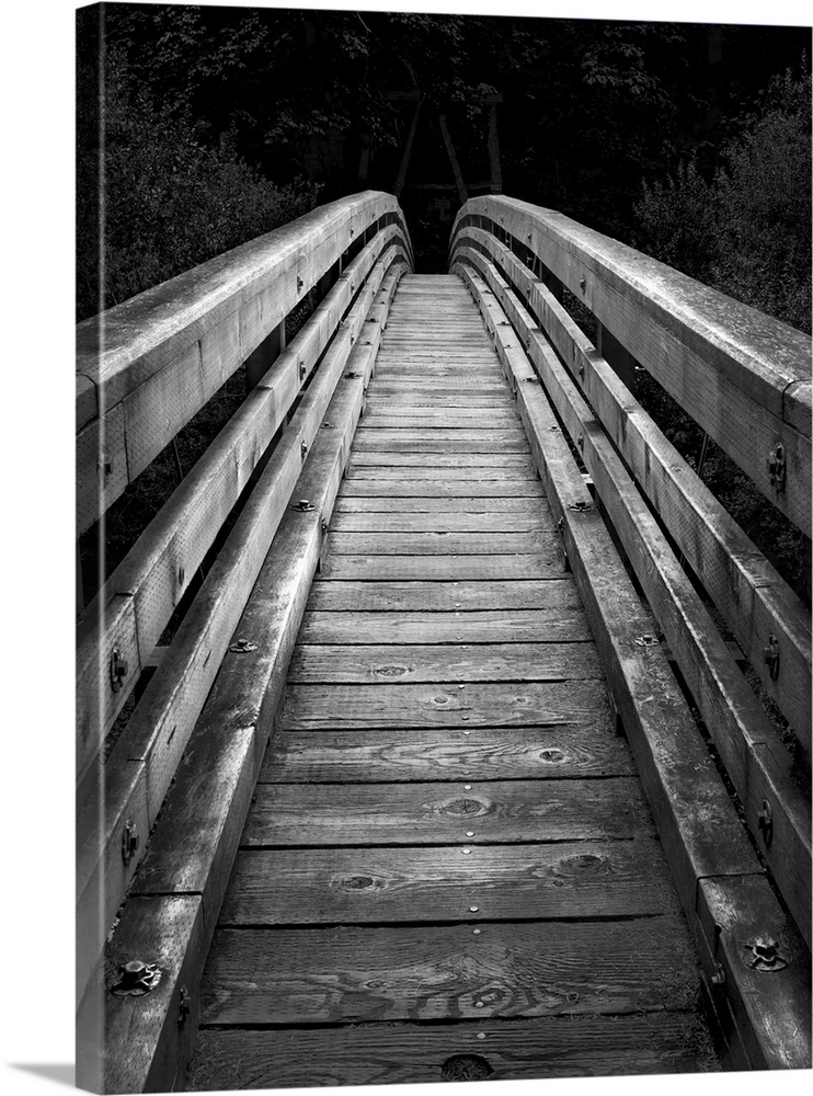 An artistic black and white photograph of of a wooden bridge with a narrow walk leading into darkness.