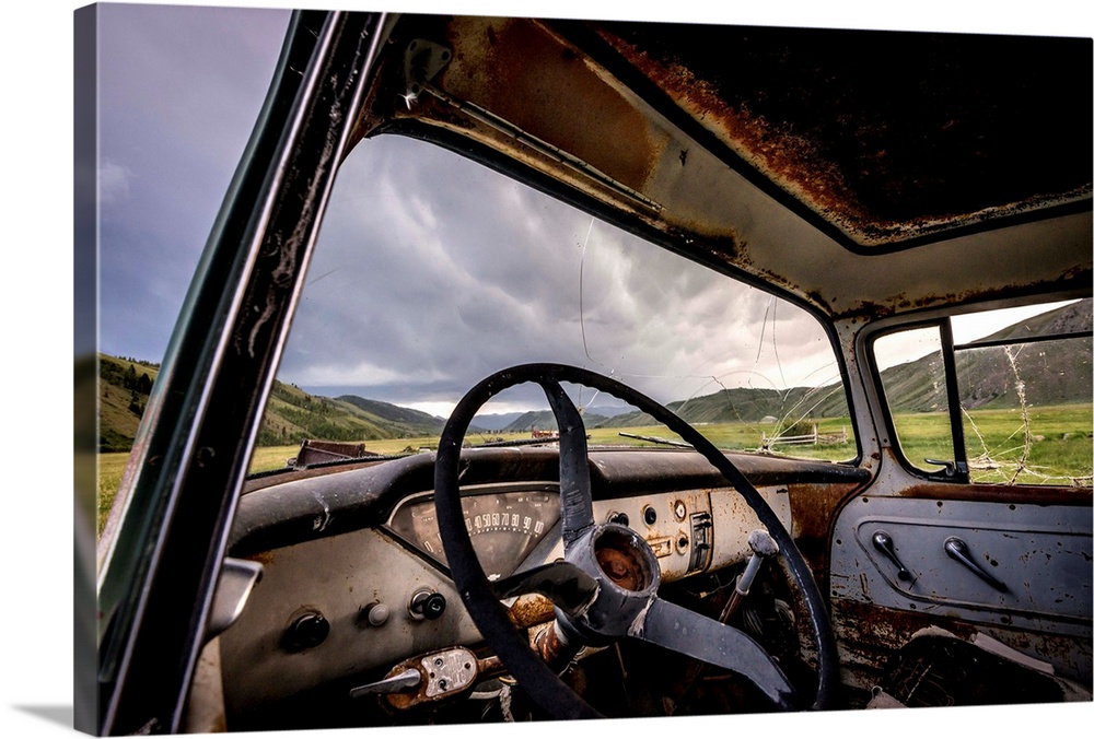 Photograph of the inside of an old abandoned car full of rust in the middle of a valley.